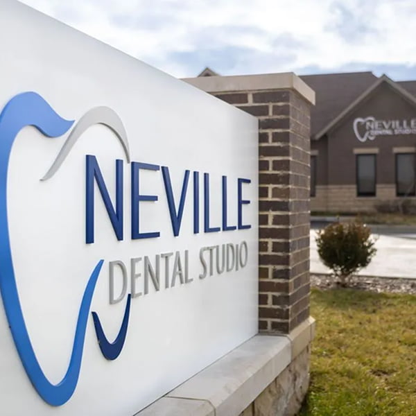 The office sign for Neville Dental Studio in a landscaped garden on a cloudy day