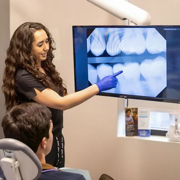 A dental assistant at Neville Dental Studio explaining an x-ray to a young patient in a modern clinical setting