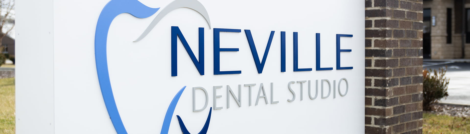 The exterior of the Neville Dental Studio building with a spacious parking lot and beautiful green landscaped gardens